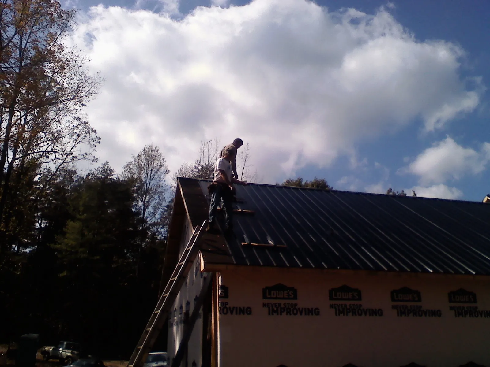 Roofer fastening dark metal panels high against a cloudy sky, from a Roof Inspection job in Hardin