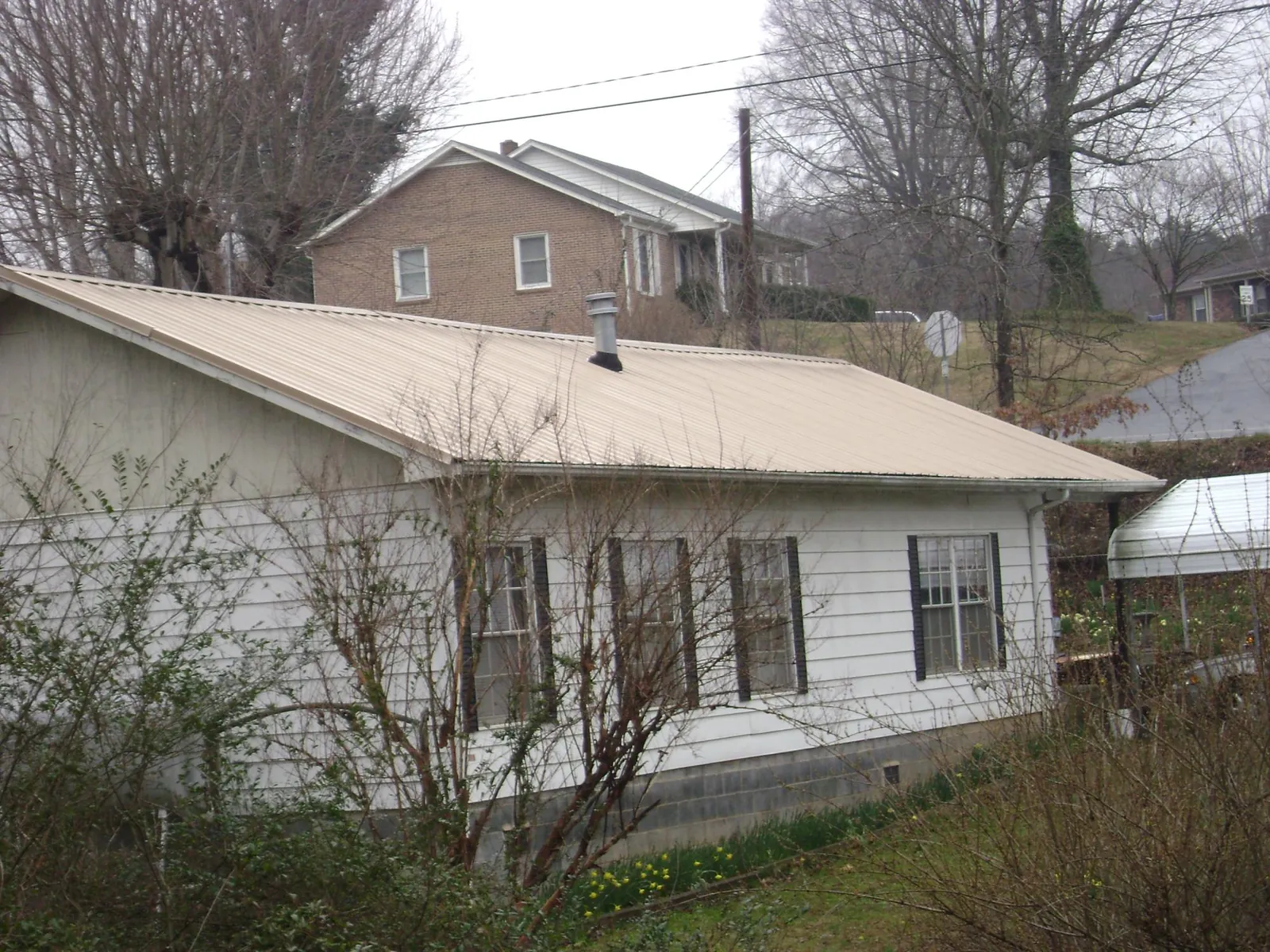 Tan metal roof on a white sided house set into a hillside — Commercial Roofing by Roofing Brothers in Hardin